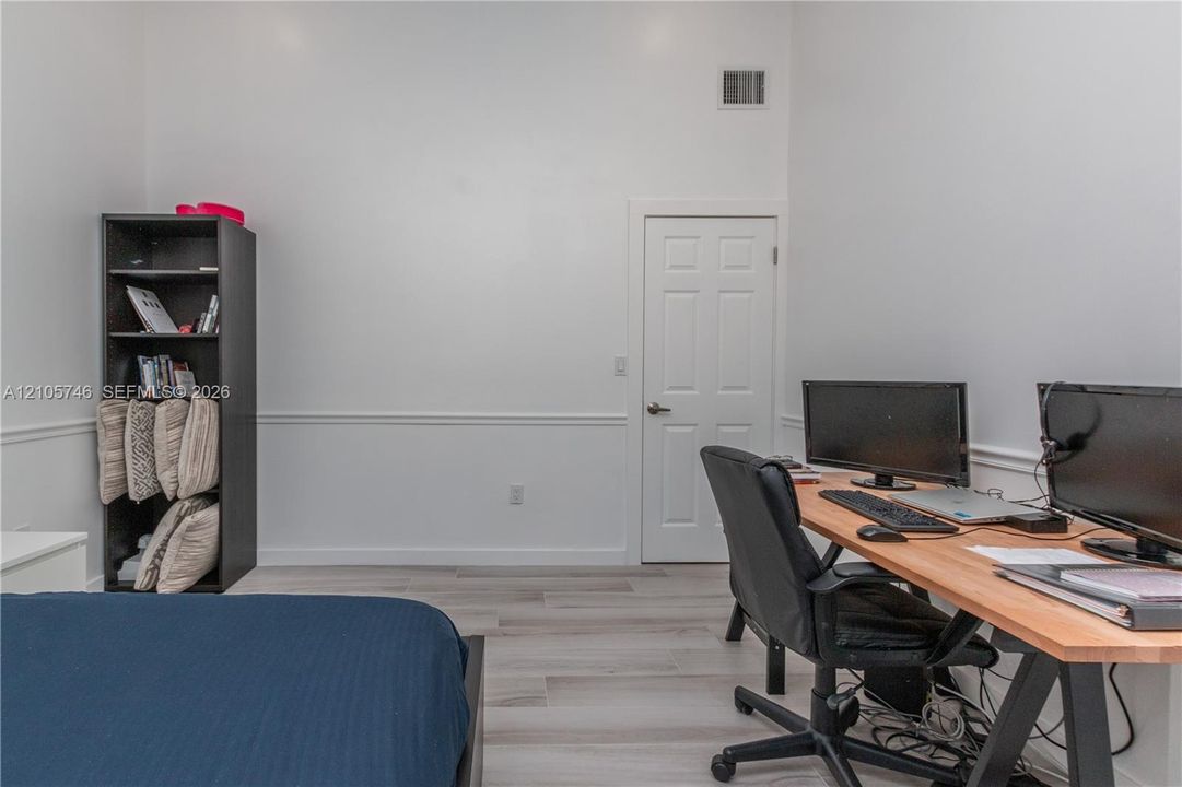 High-ceilinged room featuring light-toned wood-finish flooring, white walls, and interior chair rail molding with a six-panel door