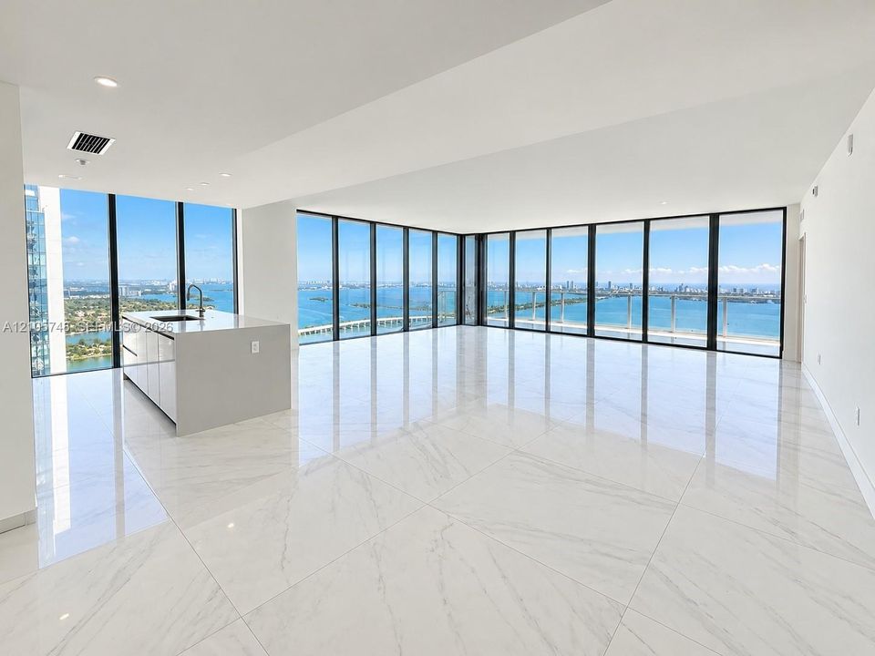Open-concept space featuring floor-to-ceiling windows, polished stone-finish tile flooring, and a kitchen island with a neutral countertop and integrated sink
