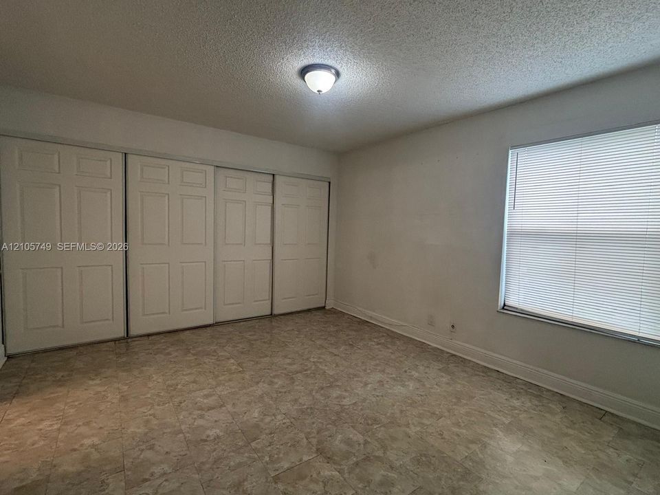 Room featuring tile flooring, four-panel sliding closet doors, and a window with horizontal blinds