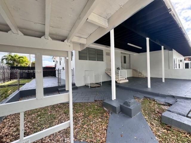 Covered patio space featuring a painted concrete floor, exposed structural beams, white support pillars, and metal stair railings
