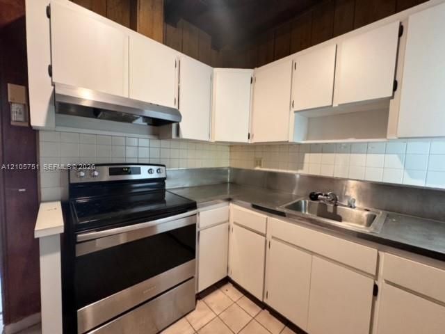 Kitchen featuring white cabinetry, stainless steel range with overhead hood, metal backsplash, and square tile flooring