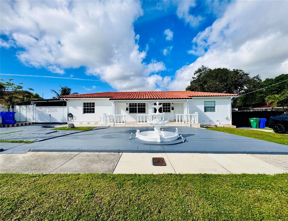 Exterior facade featuring a terracotta tile roof, white stucco finish, front-facing tiered fountain, and a paved concrete driveway