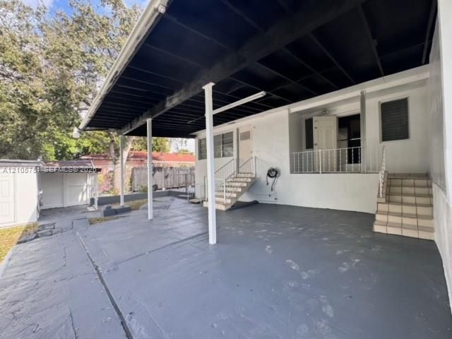 Covered concrete patio featuring painted support columns, tiered tiled staircases with metal railings, and a detached exterior storage structure
