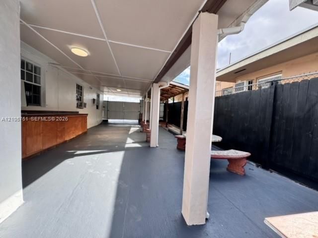 Covered patio featuring a solid-surface flooring, built-in wooden bar, support columns, and black perimeter fencing