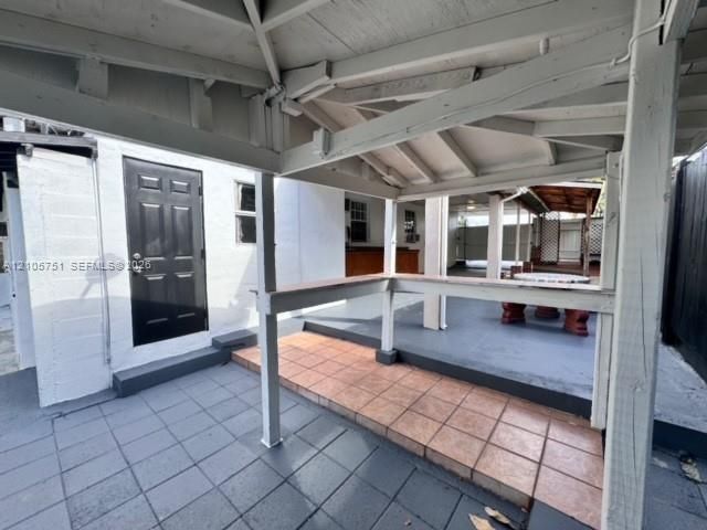 Covered patio area featuring a wooden beam structure, terracotta-style tiled flooring, and a built-in counter