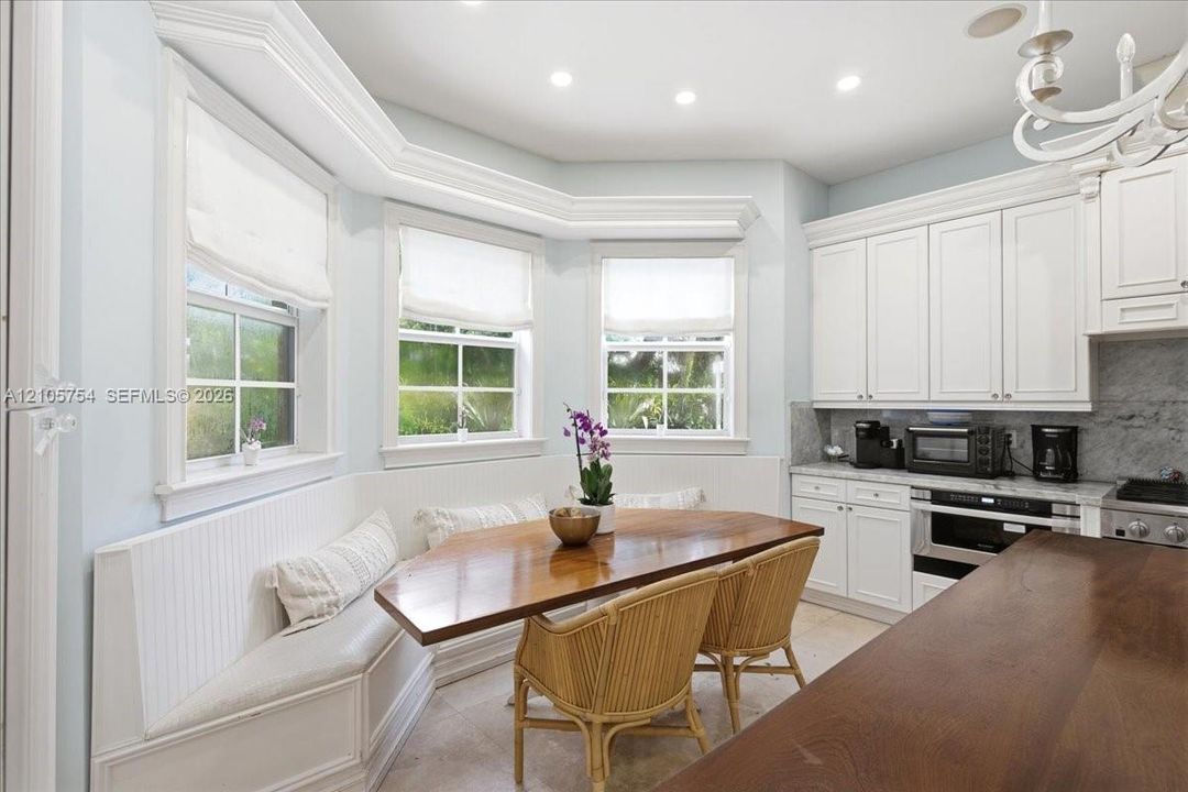 Kitchen featuring white shaker-style cabinetry, stone countertops, integrated built-in bench seating, triple-bay window configuration, and recessed ceiling lighting