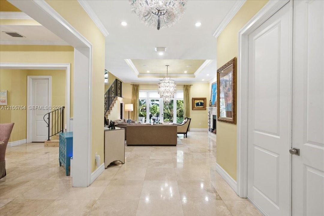 Polished stone flooring throughout, tiered tray ceilings with recessed lighting, crystal-style chandeliers, and custom crown molding