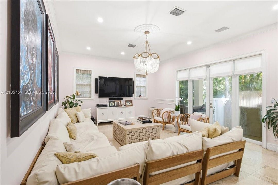 Living area featuring stone flooring, crown molding, recessed lighting, decorative ceiling medallion with a tiered chandelier, and multi-panel glass doors