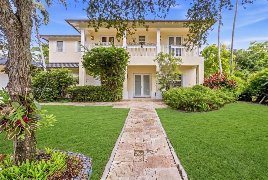 Two-story residence featuring a classic covered front porch, second-level balcony with white railings, stone-paver walkway, and manicured landscaping