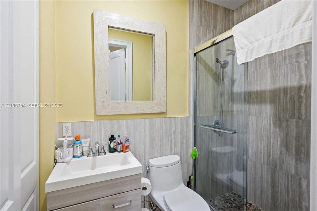 Bathroom featuring a vanity with integrated sink, rectangular mirror, walk-in shower with glass enclosure, and stone-finish wall tile