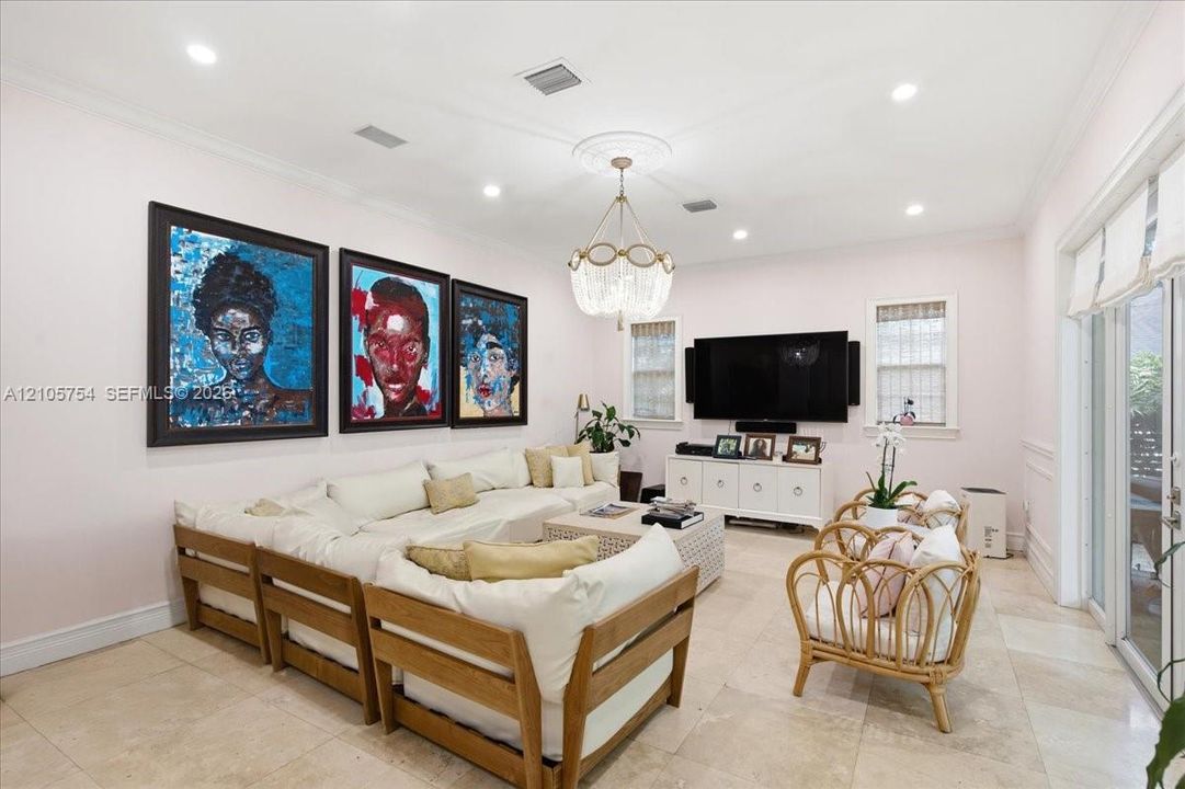 Living area featuring stone tile flooring, crown molding, a decorative ceiling medallion, an orb-style chandelier, and glass sliding doors