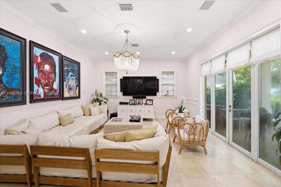 Living area featuring stone tile flooring, recessed lighting, crown molding, a decorative ceiling medallion with a tiered crystal chandelier, and floor-to-ceiling glass sliding doors