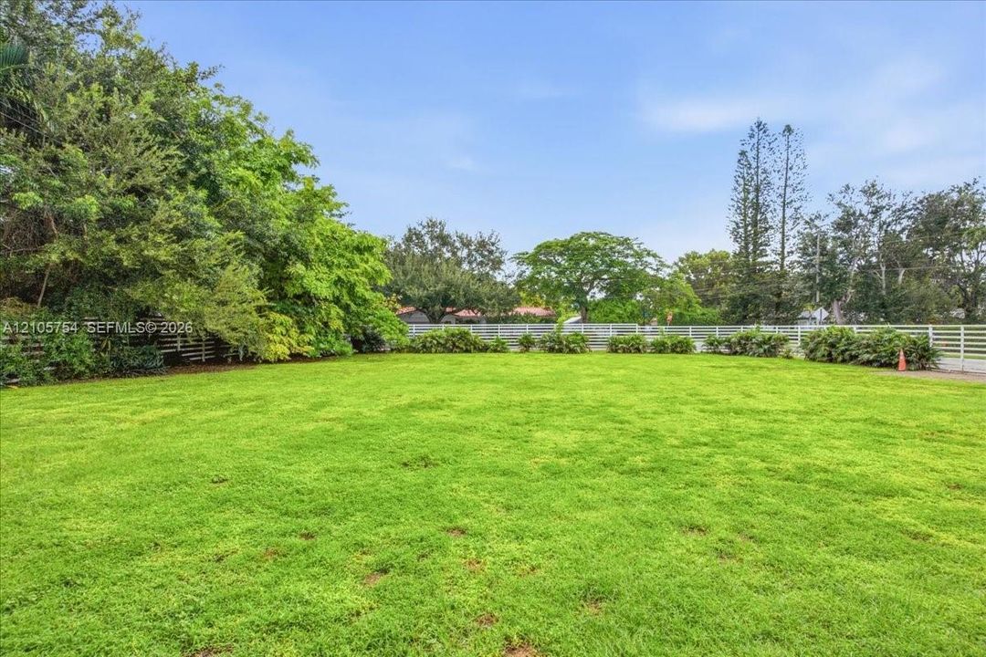 Expansive grass lawn featuring mature trees and white perimeter fencing