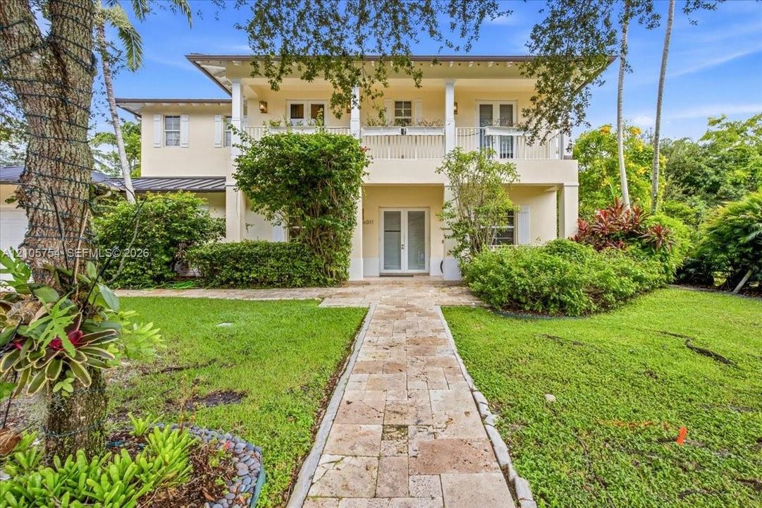 Two-story residence featuring a covered second-story balcony with white railing, stone-paver walkway, and symmetrical exterior columns