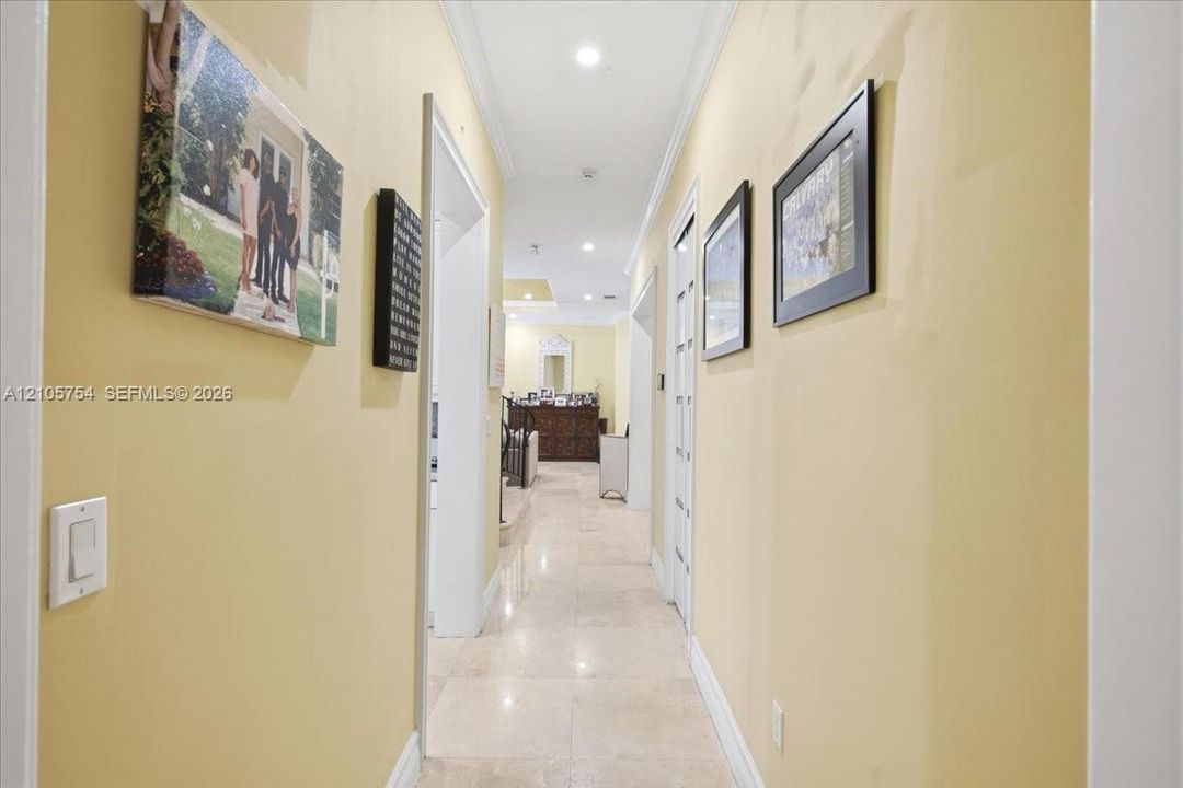 Hallway featuring light-toned stone tile flooring, recessed ceiling lighting, and crown molding