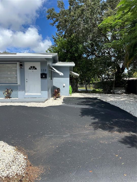 Exterior facade featuring light-colored siding, asphalt driveway, stone ground cover, and metal window awnings