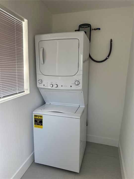 Stacked white laundry center featuring a top-load washer, a front-load dryer, and a tankless water heater