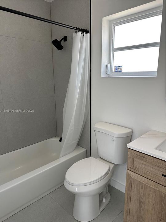Bathroom featuring large-format grey tile surround, matte black shower fixture, wood-finish vanity with countertop basin, and neutral wall tones