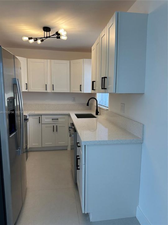 White cabinetry with black hardware, stone-composite countertops, matte black faucet, integrated stainless steel refrigerator, and multi-bulb architectural ceiling fixture