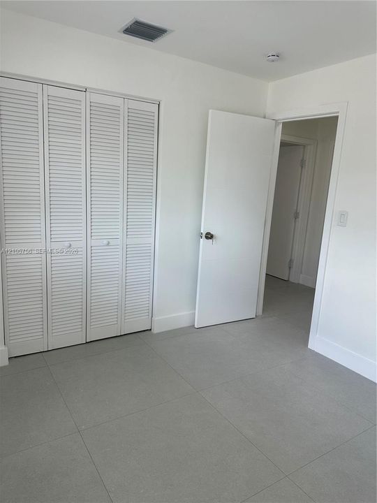 Neutral-toned large-format tile flooring, white louvered-style bi-fold closet doors, and a solid-core interior swing door with brushed metal hardware