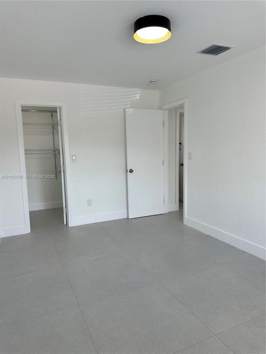 Neutral interior featuring large-format grey tile flooring, flush-mount circular lighting with a metallic rim, and built-in closet shelving