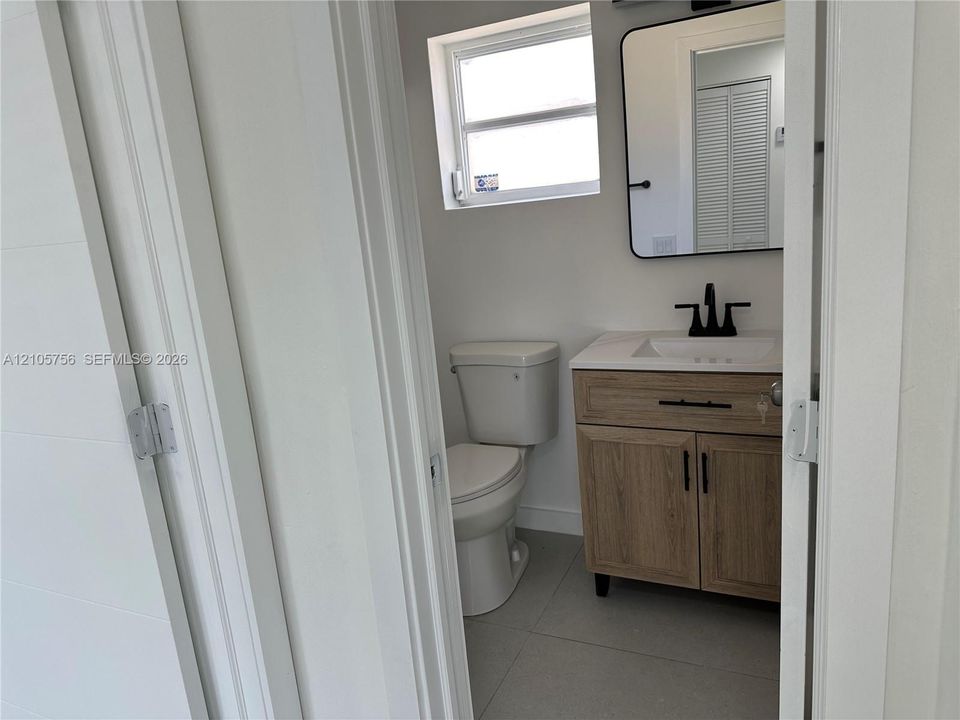 Bathroom featuring a vanity with a light wood-finish cabinet, stone-composite countertop, matte black fixtures, and a rectangular mirror with a rounded black frame