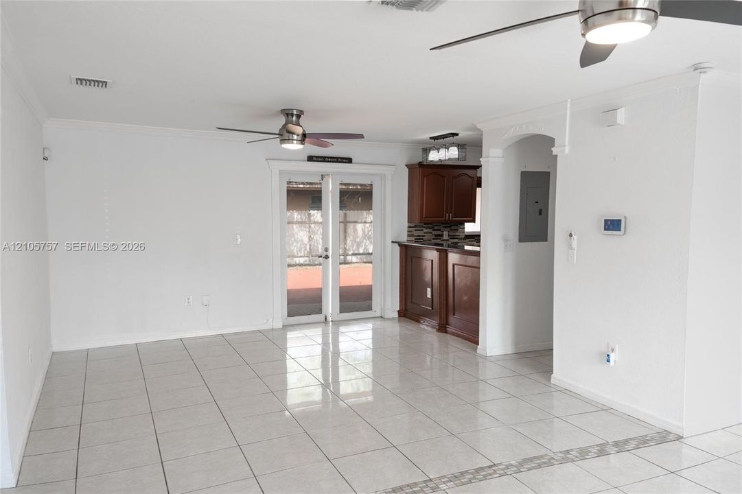 Open living space featuring tile flooring, dual ceiling fans, French doors, and a kitchen peninsula with dark-finish cabinetry