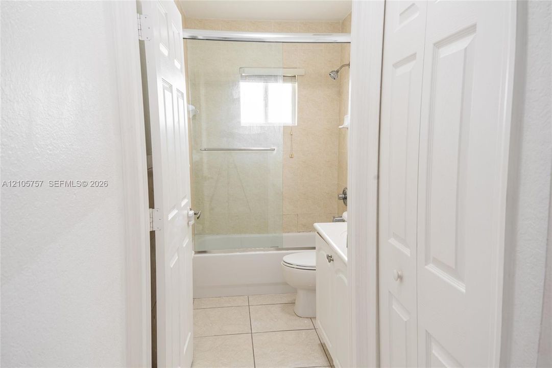 Bathroom featuring a glass-enclosed shower and tub combination, light-toned ceramic tile flooring, and a white vanity cabinet