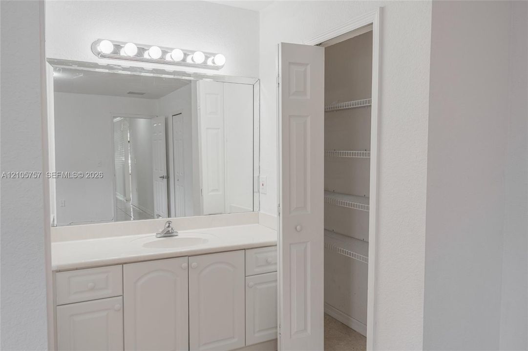 Vanity featuring an integrated sink, solid-surface countertop, multi-drawer cabinetry, wall-to-wall mirror, and multi-bulb light fixture, complemented by an integrated closet with wire shelving