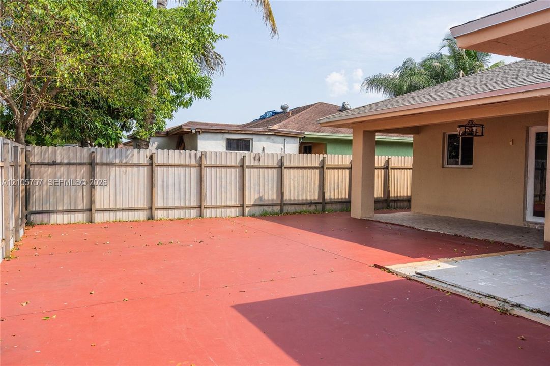 Rear exterior space featuring a covered patio, expansive concrete hardscaping, and full-height perimeter wood fencing