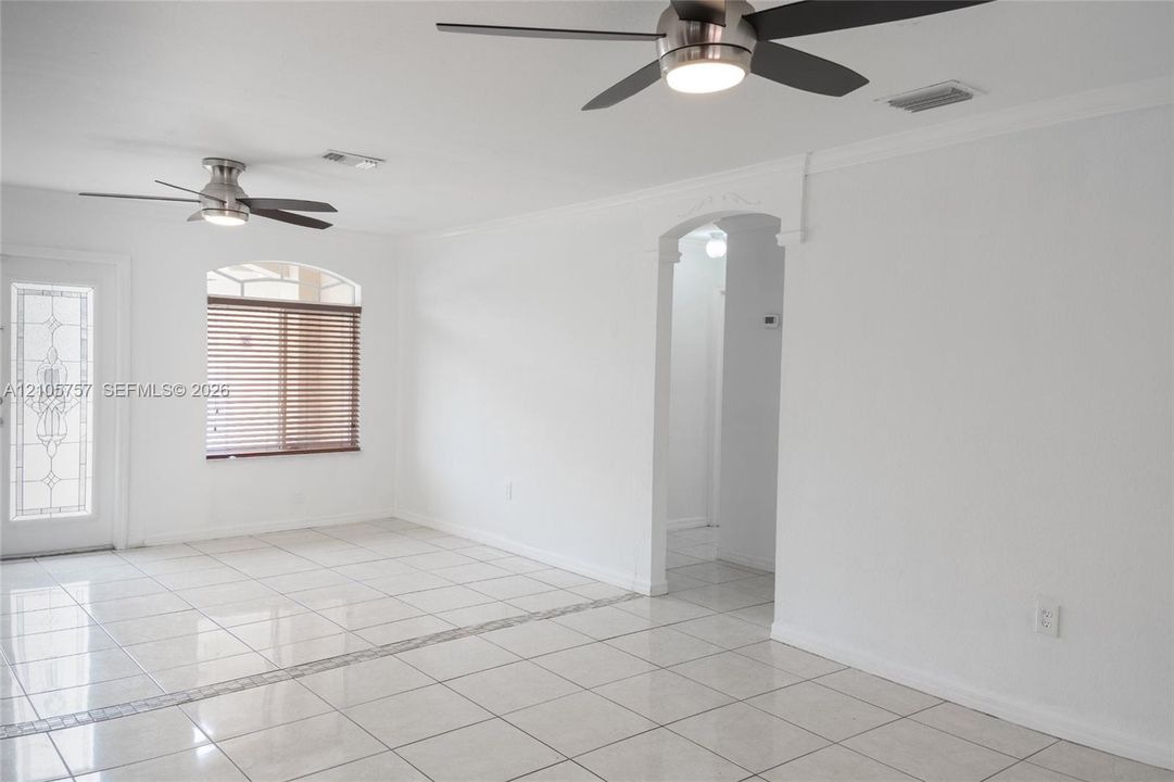 Interior space featuring neutral tile flooring, dual modern ceiling fans with integrated lighting, an arched doorway, and an exterior door with decorative glass inlay