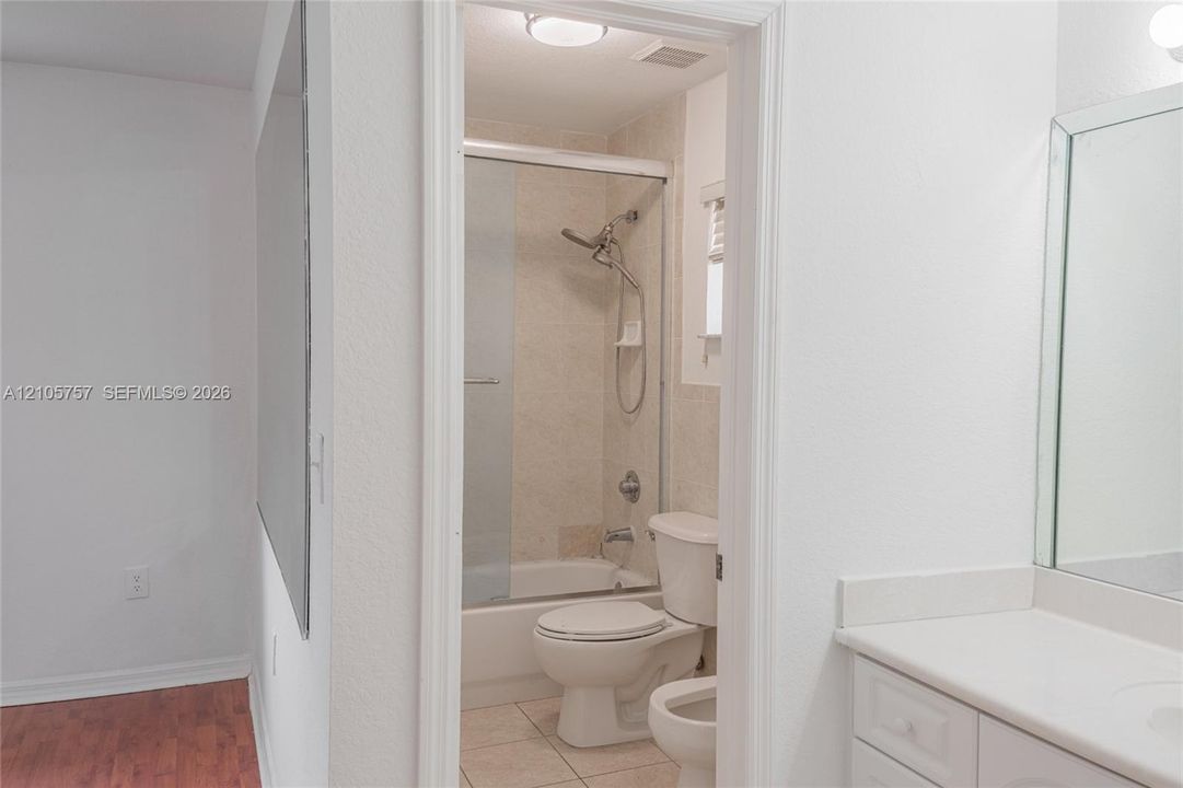 Bathroom featuring a white vanity cabinet, solid-surface countertop, rectangular wall mirror, tile flooring, and a tub-shower combination with sliding glass doors