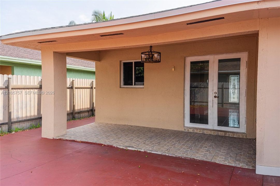 Covered patio featuring tiled flooring, a decorative metal pendant light, and French doors with glass inserts, enclosed by a solid perimeter fence