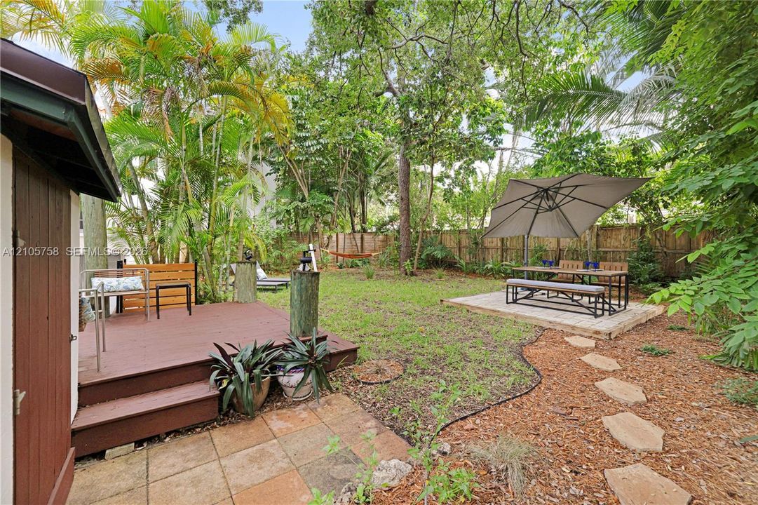 Private backyard featuring a wooden deck, stone paver patio, stone-path walkway, wood-plank fencing, and mature trees