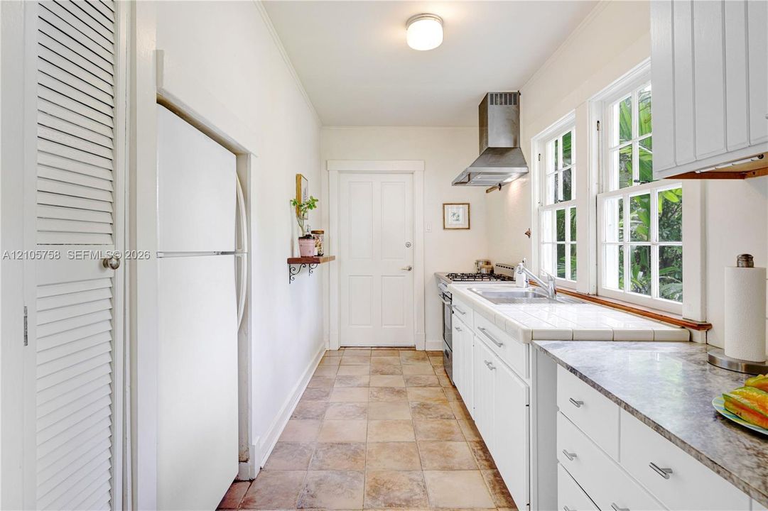 Kitchen featuring white shaker-style cabinetry, a stainless steel range hood, stone-finish countertops, tile flooring, and dual-sash windows