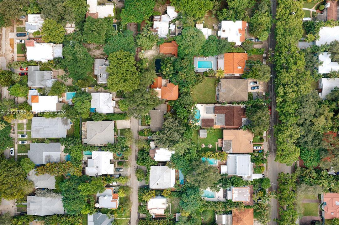 Aerial perspective of a neighborhood featuring dense tree canopy, established residential lots, varied roof pitches, and multiple private swimming pools