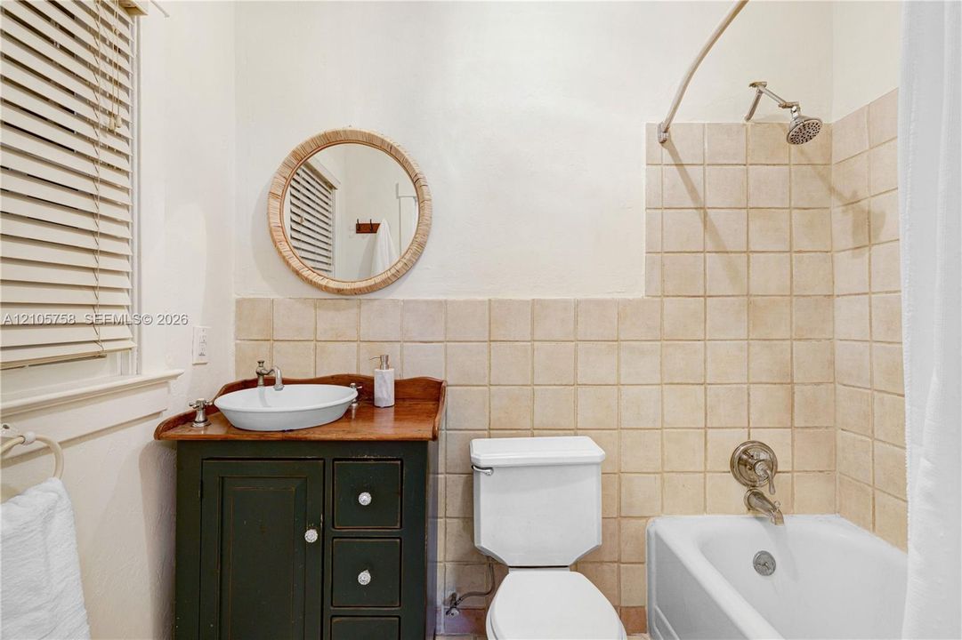 Bathroom featuring a dark-finish vanity, vessel sink, round wall-mounted mirror, and square-tile tub surround