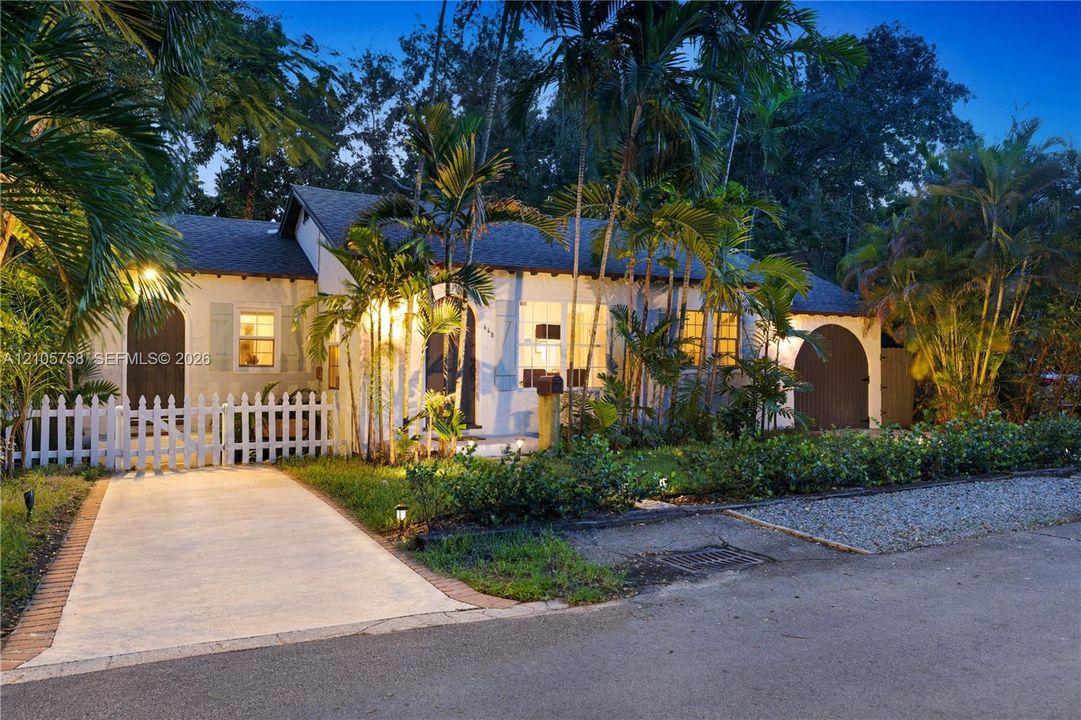 Stucco exterior featuring dual arched entryways, a white picket fence, concrete driveway, and mature palm landscaping