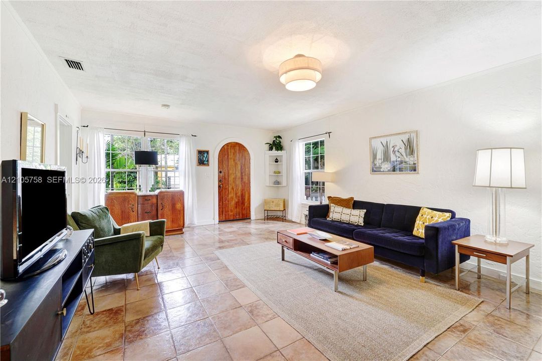 Spacious living area featuring square tile flooring, arched wooden entry door, multi-pane windows, and built-in corner shelving