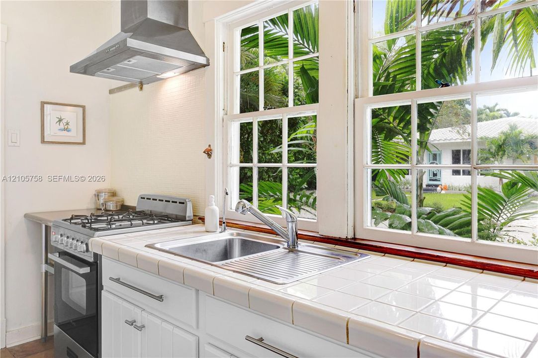 Kitchen featuring white tiled countertops, stainless steel dual-basin sink with a goose-neck faucet, freestanding stainless steel gas range, and a stainless steel vent hood