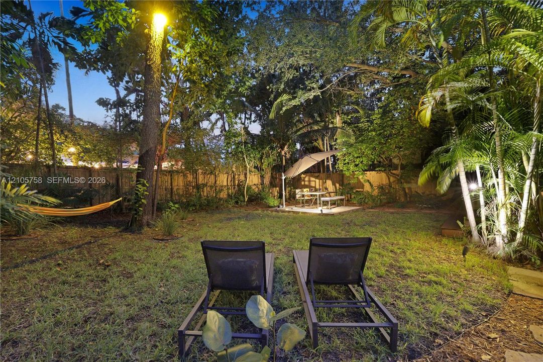 Private backyard featuring a fenced perimeter, mature trees, lush tropical landscaping, and a paved patio area
