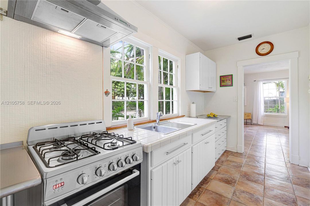 Kitchen featuring white cabinetry, tiled countertops, stainless steel gas range, stainless steel range hood, and tile flooring
