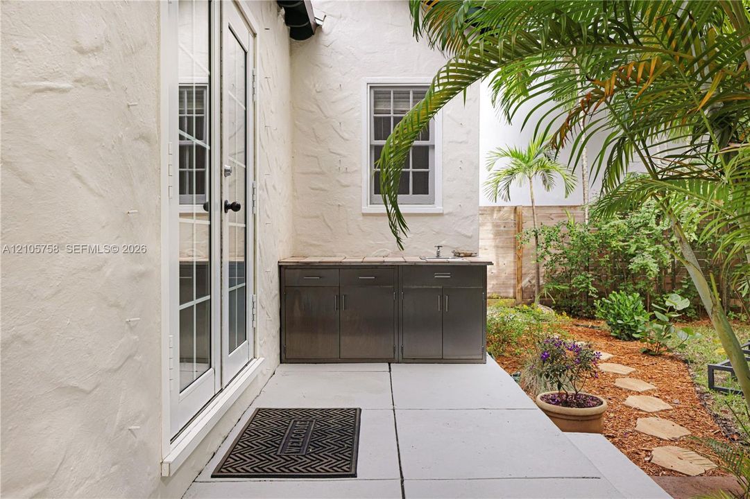 Outdoor living area featuring a paved patio, built-in stainless steel cabinetry with a stone countertop and sink, double-paned French doors, and landscaping with a stone path