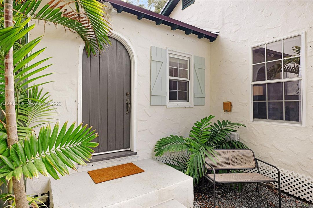 Textured stucco exterior featuring an arched entry door, paneled window shutters, and a concrete stoop