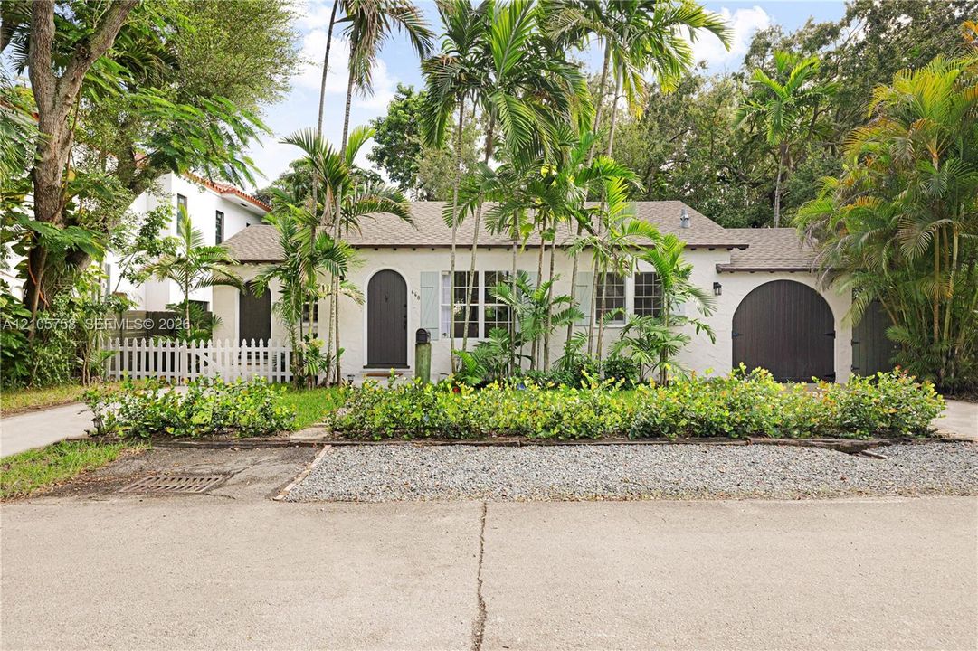 Stucco exterior featuring an arched entryway, arched garage door, shuttered windows, and a white picket fence