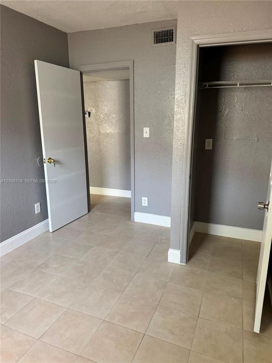Neutral-toned interior featuring square tile flooring, solid core doors with brass-finish hardware, and a built-in closet with integrated shelving