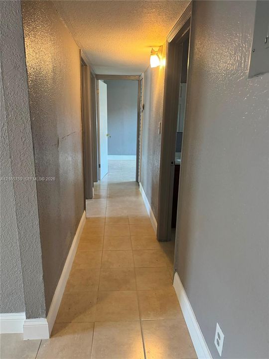 Hallway featuring neutral-toned textured wall finishes, large-format square tile flooring, and wall-mounted lighting