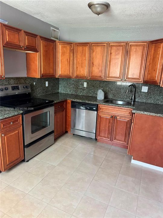 Kitchen featuring shaker-style wood cabinetry, stone countertops, stainless steel appliances, a high-arc pull-down faucet, and tiled flooring