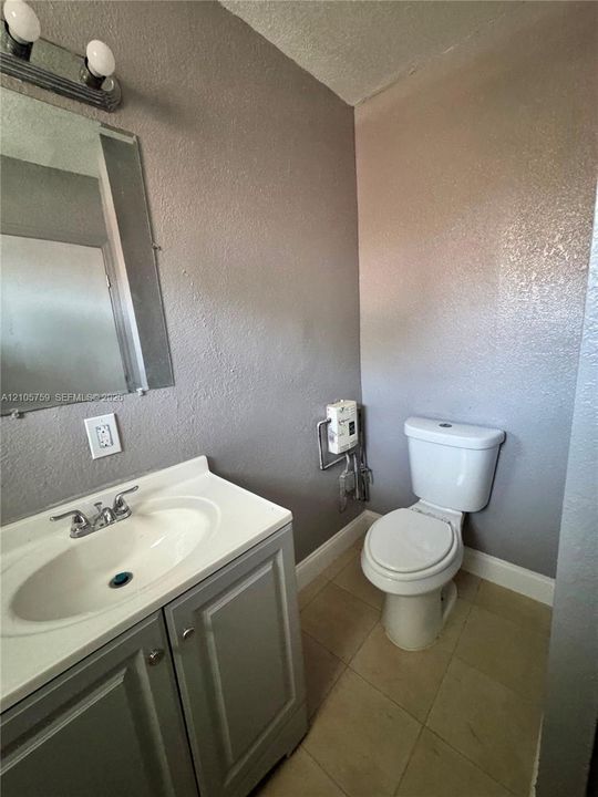 Vanity featuring a white countertop with an integrated basin, two-door cabinetry, wall-mounted mirror, and overhead light fixture, accompanied by a white porcelain toilet and tile flooring