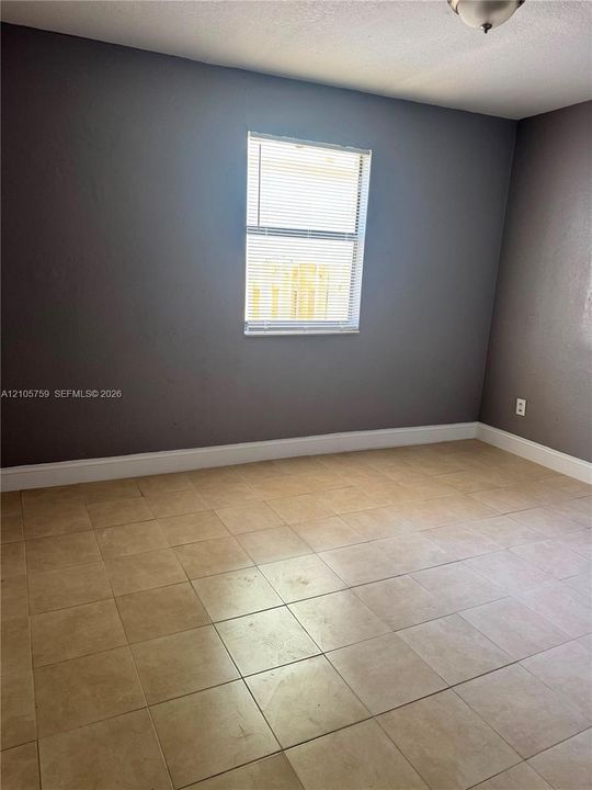 Interior room featuring neutral-toned tile flooring, gray walls, and a window with integrated blinds